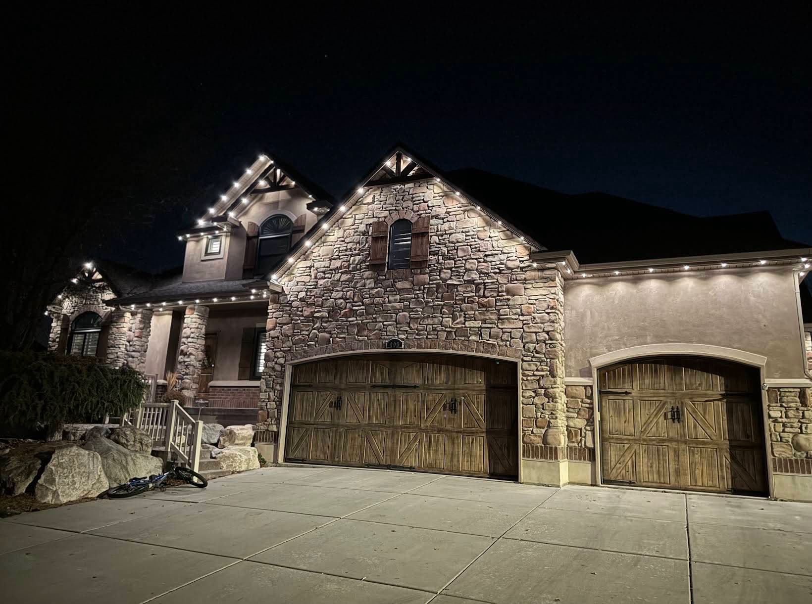 Warm-white permanent lights accenting stonework and garage rooflines